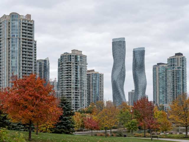 Residential condo towers in Mississauga City Centre seen across a park with autumn trees, including two curving white towers